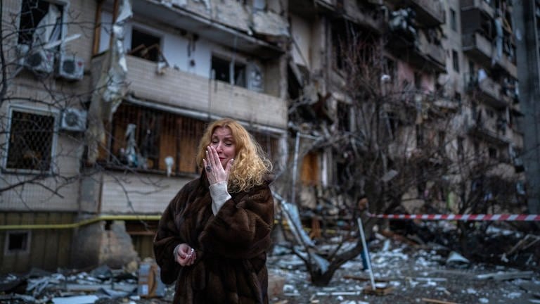 Eine Frau neben ihrem Haus in Kiew in der Ukraine nach einem Raketenangriff. Russland hat am 24. Februar 2022 einen umfassenden Angriff auf die Ukraine gestartet und Städte und Stützpunkte mit Luftangriffen oder Granaten beschossen. (Foto: dpa Bildfunk, picture alliance/dpa/AP | Emilio Morenatti)