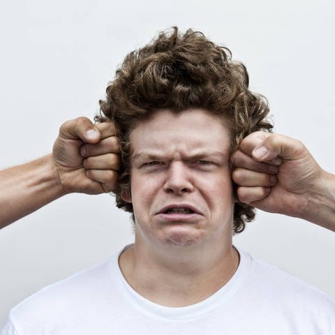 Zwei Fäuste attackieren den Kopf eines jungen Mannes: Eine Definition von Gewalt ist: Es handelt sich um Absicht, ist kein Versehen oder ein Unfall (Foto: IMAGO, IMAGO / imagebroker)