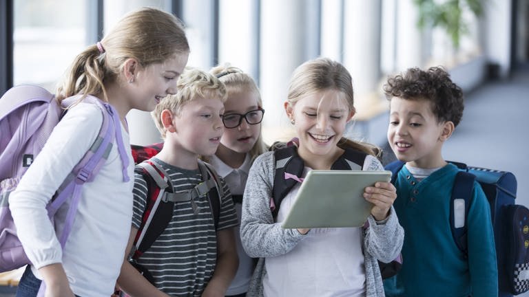 Kinder schauen im Schulkorridor in ein Tablet (Foto: IMAGO, imago/Westend61)