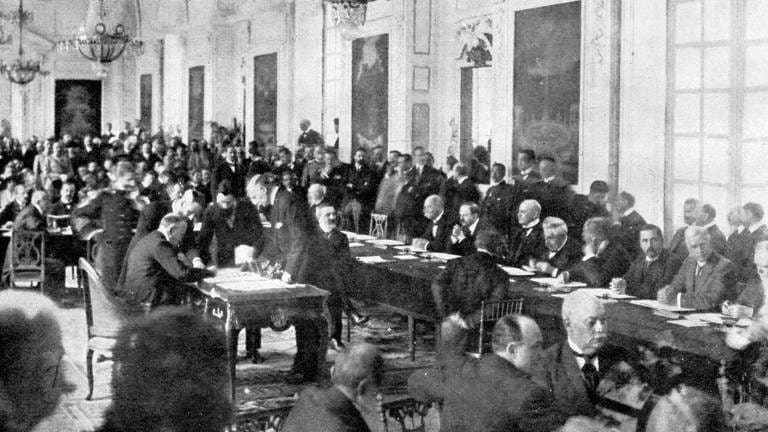 Unterzeichnung des Friedensvertrages mit Ungarn im Trianon in Versailles am 12. Juni 1920: Der italienische Botschafter in Paris setzt seine Unterschrift auf das Dokument (Foto: IMAGO, imago images / United Archives International)