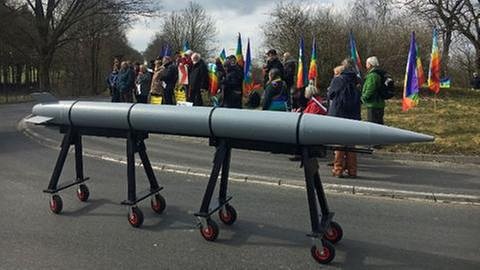 Eine große gebastelte Rakete und dahinter stehen Friedensaktivisten (Foto: SWR, SWR -)