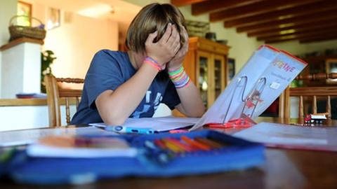 Junge sitzt am Wohnzimmertisch über seine Hausaufgaben gebeugt, stützt den Kopf erschöpft in die Hände (Foto: picture-alliance / dpa, picture-alliance / dpa - Julian Stratenschulte)