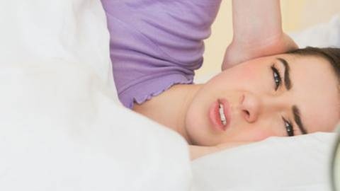 Frau wird unsanft vom Wecker-Klingeln in ihrem Bett überrascht und  hält sich die Ohren zu. (Foto: Getty Images, Thinkstock -)