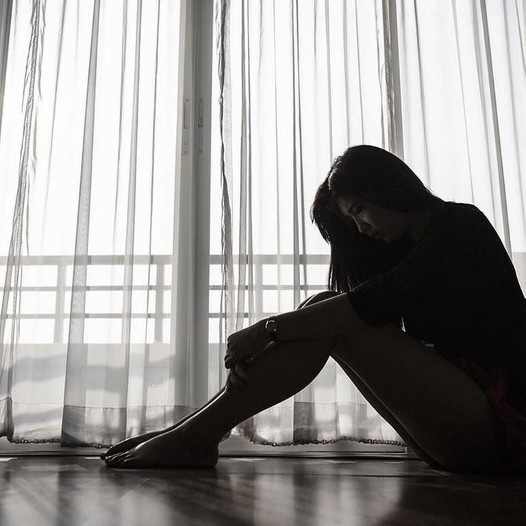 Eine Frau sitzt auf dem Fußboden vor dem Fenster (Foto: Getty Images, Thinkstock -)