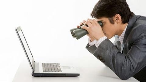 Mann starrt mit Fernglas auf einen Laptop. (Foto: Getty Images, Thinkstock -)