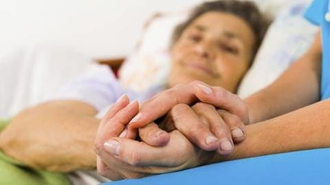 Eine Krankenschwester hält die Hand einer älteren Frau (Foto: Getty Images, Thinkstock -)