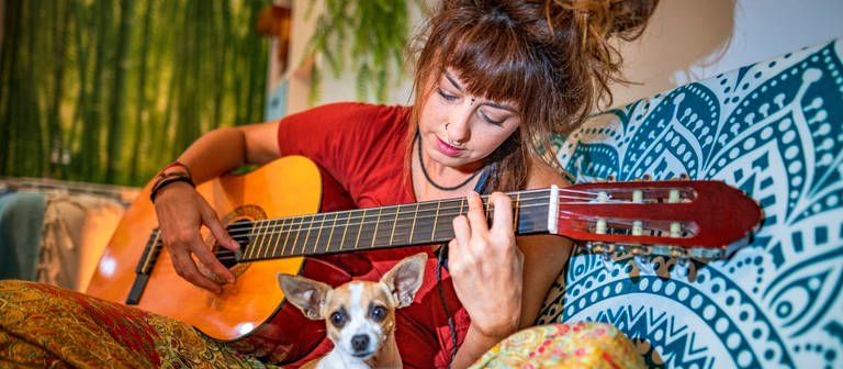 Eine junge Frau spielt Gitarre: Musikwissenschaftlerinnen und Hirnforscher versuchen in der Musik Merkmale zu identifizieren, die bei allen Menschen eines Kulturkreises oder sogar weltweit dieselben Gefühle auslösen (Foto: IMAGO, IMAGO / Westend61)