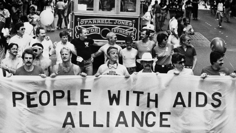 Demonstranten tragen während der 13. jährlichen Gay Freedom Day Parade am 27. Juni 1983 in San Francisco ein Banner mit der Aufschrift "People With Aids Alliance" (Foto: picture-alliance / Reportdienste, picture alliance / AP Images)