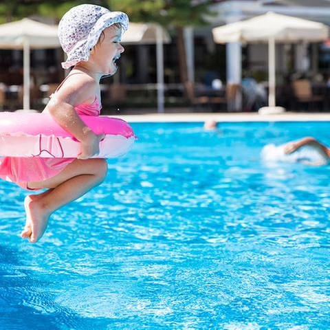 Ein kleines Mädchen mit Schwimmring hüpft in das Becken in einem Schwimmbad. (Foto: Getty Images, Thinkstock -)