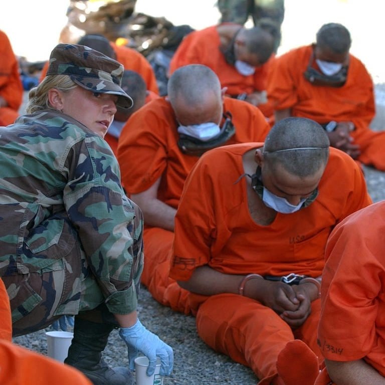 Eine US-Militärpolizistin versorgt angekettete Häftlinge mit Wasser, als dise am 12. Feburar 2002 im Marinestützpunkts Guantanamo Bay ankommen. Das US-Militär geht davon aus, dass die Gefangenen mit Al-Qaida oder den Taliban in Verbindung stehen. (Foto: picture-alliance / Reportdienste, picture alliance / Everett Collection | SGT DIANA RUIZ)