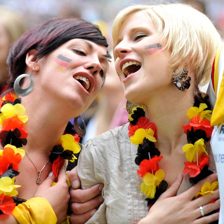 Zwei junge Frauen mit Blumenkette in Deutschland-Farben und der Hand auf dem Herzi singen beim Fußballspiel in Düsseldorf 2010 die Nationalhymne (Foto: dpa Bildfunk, picture alliance / dpa | Rene Tillmann)