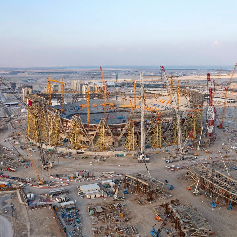 Planstadt Lusail bei Doha: Das Fußball-Stadion bietet Platz für 80.000 Zuschauer (Drohnehfoto von der Baustelle): Etliche Stadien in Katar sind klimatisiert, die staatseigene Fluglinie gehört zu den wichtigsten Sponsoren im Fußball. Abseits von Katar diskutiert die Sportindustrie zunehmend über Klimaschutz. Doch das Umweltbewusstsein im Profi-Fußball ist eher gering. (Foto: IMAGO, IMAGO / MIS)