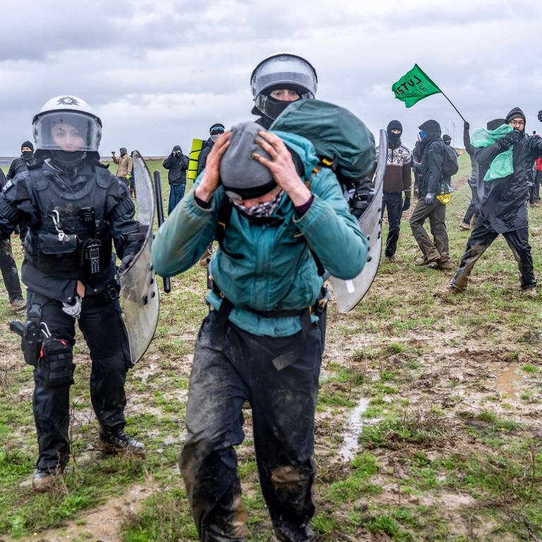 Zwei Polizisten in Schutzkleidung verfolgen einen Demonstranten auf einem Feld bei Lützerath (Foto: IMAGO, Jochen Tack)