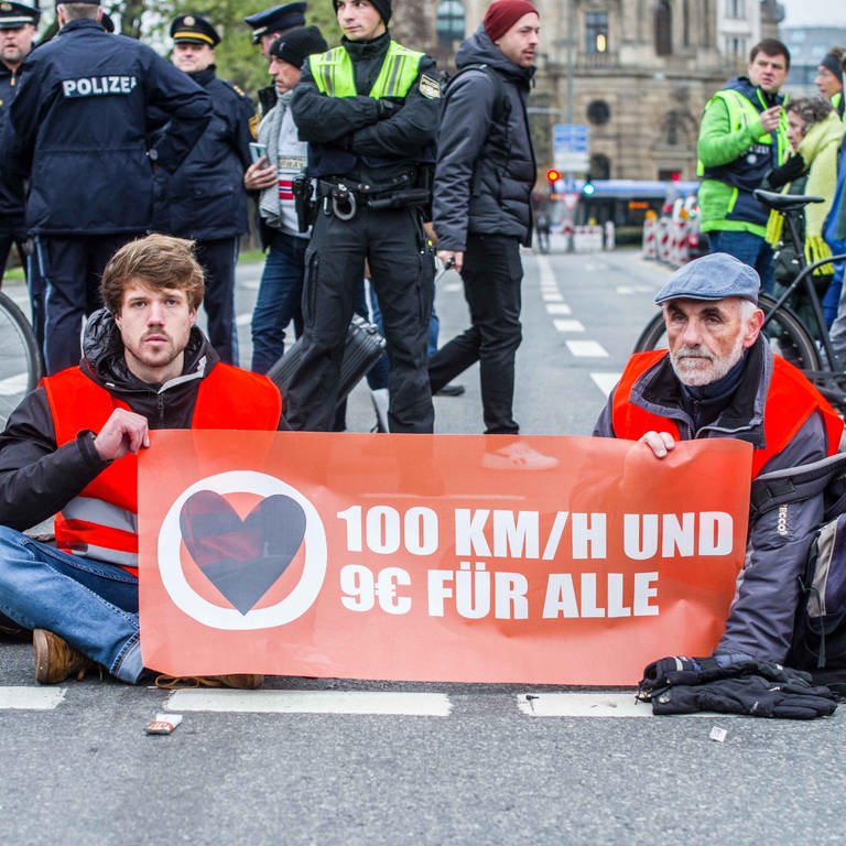 Klima-Aktivisten der "Letzten Generation" haben sich am Karlsplatz in München festgeklebt. Auf einem Transparent steht "100 kmh und 9 € für alle" (Foto: picture-alliance / Reportdienste, picture alliance / ZUMAPRESS.com | Sachelle Babbar)