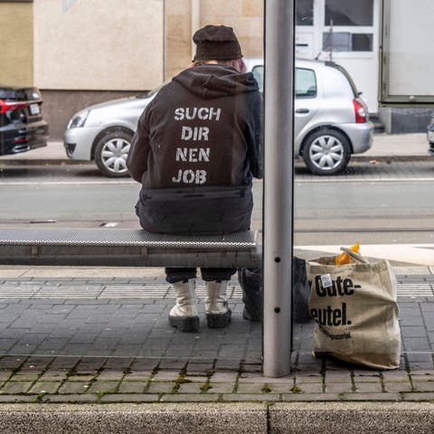 Person sitzt an einer Bushaltestelle, Hoodie mit der Aufschrift: "Such dir nen Job" (Foto: IMAGO, IMAGO / Jochen Tack)
