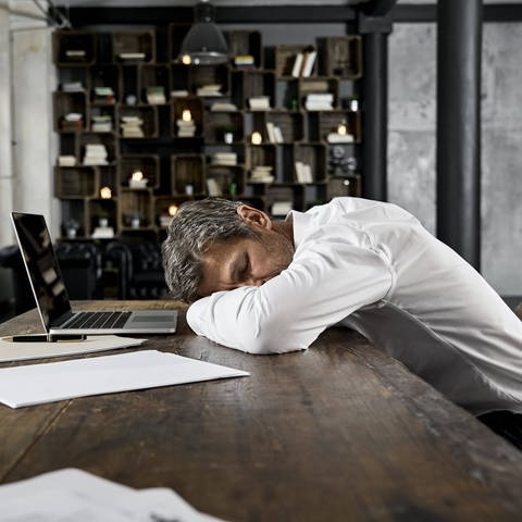 Symbolfoto: Geschäftsmann, der auf Schreibtisch im Loftmodell schläft (Foto: IMAGO, IMAGO / Westend61)