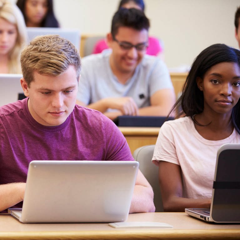 Ein junger Mann sitzt in einem Hörsaal der Universität mit aufgeklapptem Laptop neben anderen Studierenden (Foto: IMAGO, IMAGO / Shotshop)