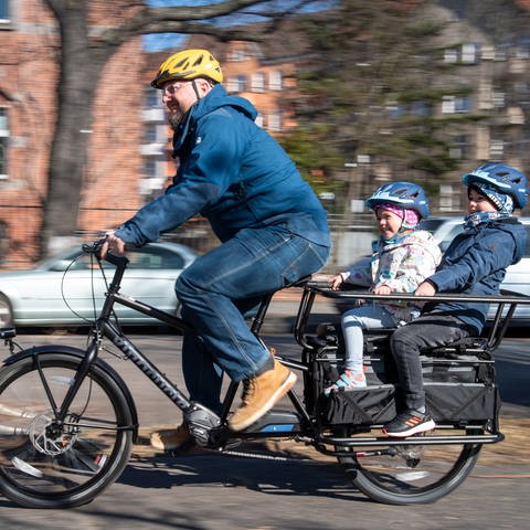 Ein Vater fährt seine Kinder mit einem Lastenrad (Foto: picture-alliance / Reportdienste, picture alliance / dpa-tmn | Zacharie Scheurer)
