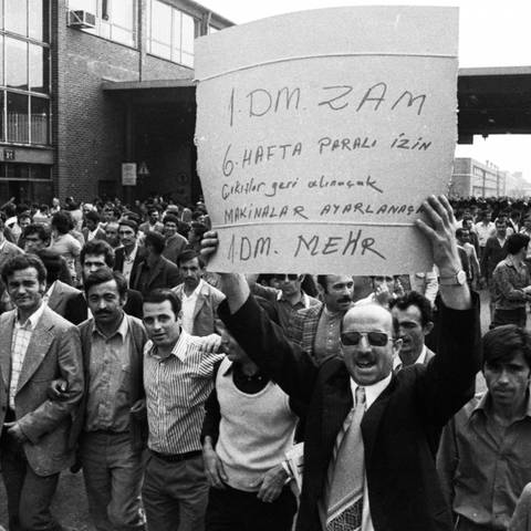 Der Streik bei den Ford-Werken, hier am 27. bis 29. 8. 1973 in Köln, war ein Spontanstreik, also ein wilder Streik. Die Serie von Streiks wurde u. von türkischen Migranten organisiert. Ursache war u. a. die starke Inflation. Auf dem Schild in türkischer Sprache, das einer der Männer in die Höhe hält, steht in der letzten Zeile auf Deutsch "1 DM mehr". (Foto: picture-alliance / Reportdienste, picture alliance / imageBROKER | klaus Rose)