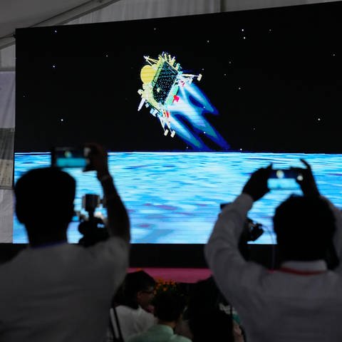 Journalisten filmen die Live-Übertragung der Landung des Raumschiffs «Chandrayaan-3» auf dem Mond in der ISRO-Einrichtung für Telemetrie, Ortung und Kommandonetz. (Foto: picture-alliance / Reportdienste, picture alliance/dpa/AP | Aijaz Rahi)