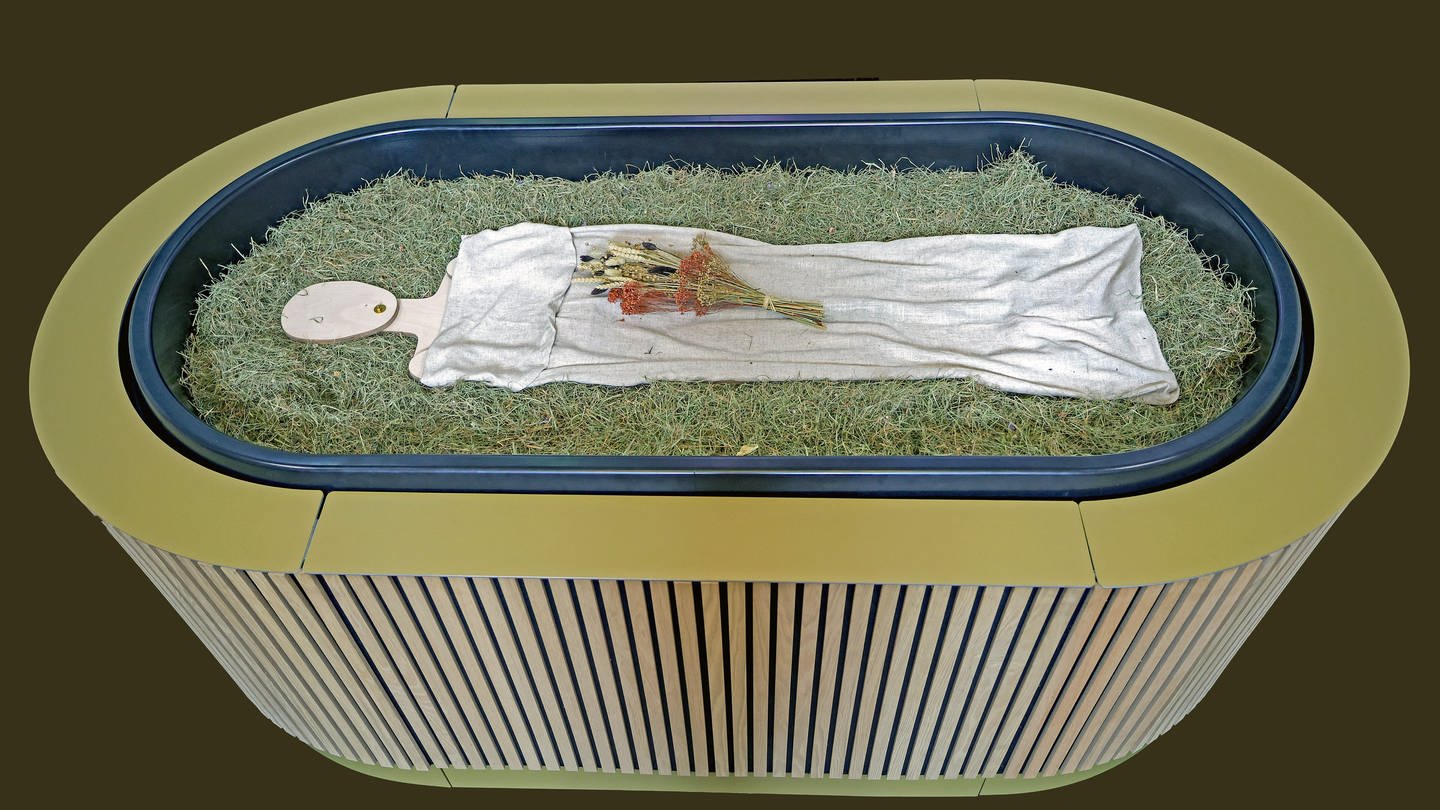 Heu, Stroh, Blumen und eine Holzfigur liegen in einem sogenannten „Kokon“ bei einem Pressegespräch zu der neuen Bestattungsform 