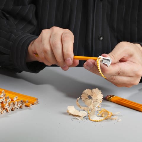 Man sharpening a heap of pencils with a pencil sharpener Symbolfoto (Foto: IMAGO, YAY Images)