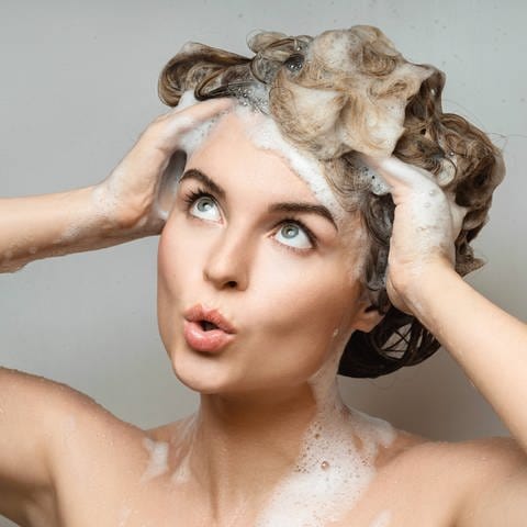 IMAGO  Zoonar (Foto: IMAGO, Junge Frau wäscht sich die Haare: Bio ist bei Naturkosmetik nicht so klar geregelt wie bei Lebensmitteln. Neben Zusatzstoffen ist beim Shampoo auch die Energiebilanz wichtig.)