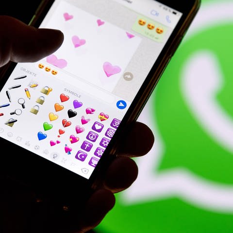 Ein Smartphone mit Emojis aus WhatsApp vor dem WhatsApp-Logo (Foto: picture-alliance / Reportdienste, picture alliance / Fabian Sommer/dpa | Fabian Sommer)
