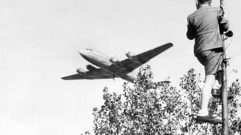 Berliner Luftbrücke: Ein Junge verfolgt von einem Baum aus den Landeanflug eines US-amerikanischen Transportflugzeugs auf den Berliner Flughafen Tempelhof.  (Foto: picture-alliance / Reportdienste, dpa)