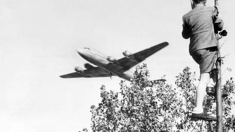 Berliner Luftbrücke: Ein Junge verfolgt von einem Baum aus den Landeanflug eines US-amerikanischen Transportflugzeugs auf den Berliner Flughafen Tempelhof.  (Foto: picture-alliance / Reportdienste, dpa)