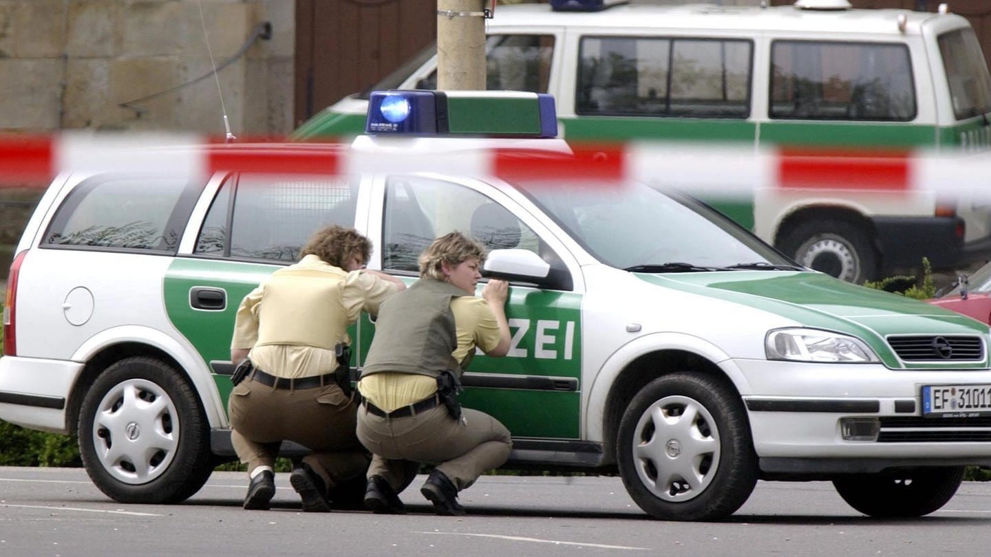 In Deckung gehen Polizeibeamtinnen hinter ihrem Wagen am Freitag, 26. April 2002 vor dem Gutenberg-Gymnasium in Erfurt. In einem  Amoklauf hat ein ehemaliger Schüler in diesem Gymnasium 17 Menschen und sich selbst erschossen. Mindestens vier Menschen wurden verletzt.
