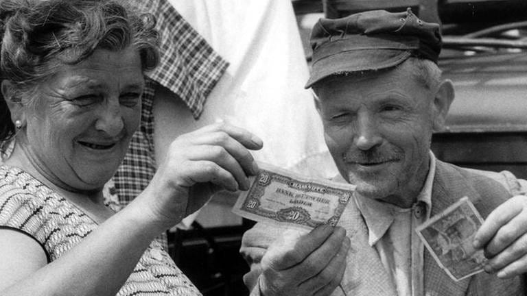 Ein Ehepaar vergleicht am 6. Juli 1959 auf dem Saarbrücker Markt alte und neue Geldscheine (Foto: picture-alliance / dpa, picture-alliance / dpa -)