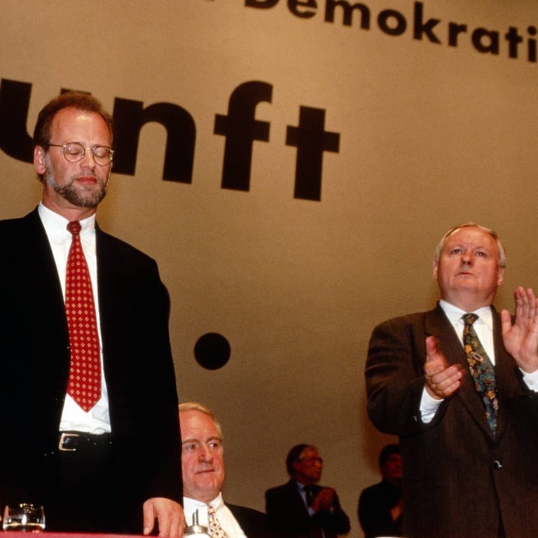 Der geschlagene und abgewählte Rudolf Schwarping (links) nimmt den Applaus von Oskar Lafontaine entgegen auf dem Parteitag der SPD am 16.11.1995 in Mannheim. In der Mitte Johannes Rau. (Foto: IMAGO, imago/Rainer Unkel)