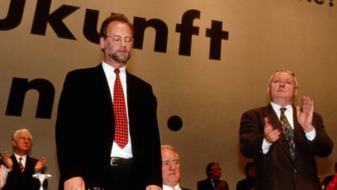 Der geschlagene und abgewählte Rudolf Schwarping (links) nimmt den Applaus von Oskar Lafontaine entgegen auf dem Parteitag der SPD am 16.11.1995 in Mannheim. In der Mitte Johannes Rau. (Foto: IMAGO, imago/Rainer Unkel)
