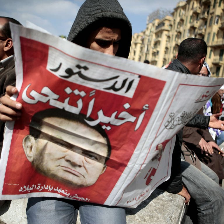 Husni Mubarak ist zurückgetreten; ein Mann liest die Meldung in der Zeitung. Menschen feiern am 12. Februar auf dem Tahrir-Platz in Kairo  Ägypten (Foto: picture-alliance / Reportdienste, picture alliance / abaca | De Malglaive Etienne)