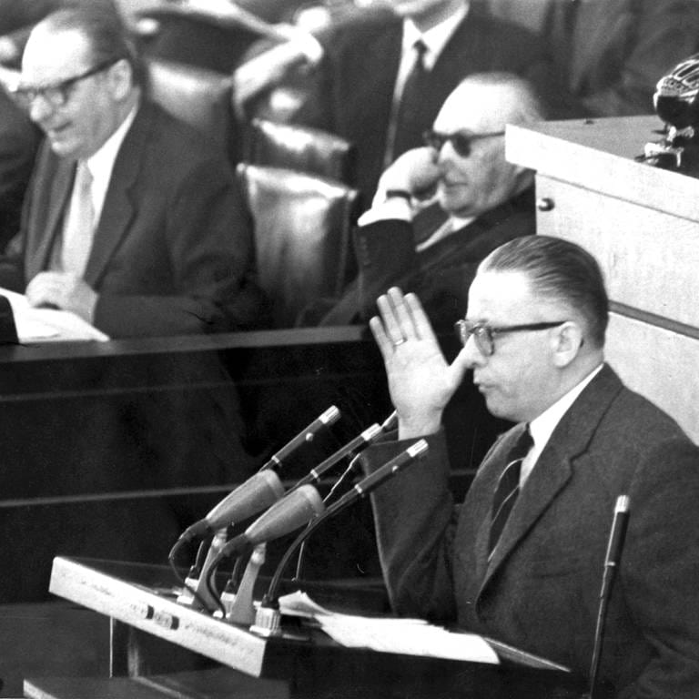 Der SPD-Abgeordnete Dr. Gustav Heinemann als erster Redner des Tages während der Fortsetzung der großen außenpolitischen Debatte im Deutschen Bundestag in Bonn am 25.3.1958. Im Hintergrund Bundeskanzler Konrad Adenauer (mit Sonnenbrille), Außenminister Heinrich von Brentano (M) und Justizminister Fritz Schäffer. Heinemann lehnte in seiner Rede die Fragestellung des Bundeskanzlers, NATO oder nicht, als Kernpunkt der Politik ab. Vor einer Sitzungspause am vorangegangenen Wochenende war im Bundestag bereits 28 Stunden lang leidenschaftlich über die politische Situation der Bundesrepublik, die Wiedervereinigung und die atomare Ausrüstung der Bundeswehr debattiert worden. (Foto: picture-alliance / Reportdienste, picture-alliance / dpa | Rohwedder)