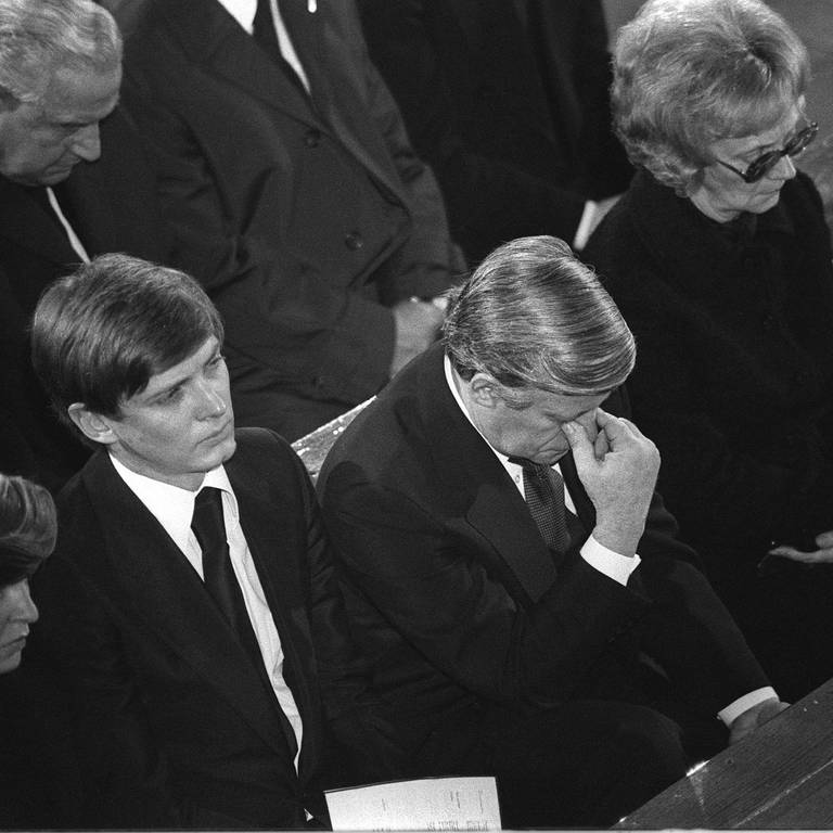 Trauerfeier für Hanns Martin Schleyer am 25.10.1977 in Stuttgart: Bundeskanzler Helmut Schmidt mit gesenktem Kopf; links neben ihm Schleyers ältester Sohn Eberhard, rechts von ihm Schleyers Witwe Waltrude (Foto: picture-alliance / Reportdienste, picture-alliance / Sven Simon | Rauchensteiner/SVEN SIMON)