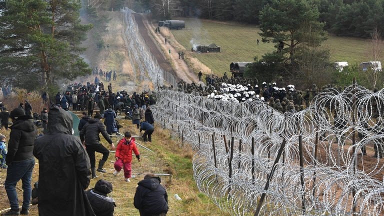 Polnische Polizisten und Soldaten (rechts) bewachen am 8.11.2021 die Grenze in der Nähe eines Migrantenlagers an der weißrussisch-polnischen Grenze in der Region Grodno  Belarus. Hunderte von Migranten aus dem Nahen Osten und Nordafrika versuchten, die Grenze von Weißrussland nach Polen zu überwinden. Aus Sicht der EU benutzt Belarus die Flüchtlinge, um Druck auf die EU auszuüben. (Foto: IMAGO, IMAGO / SNA)