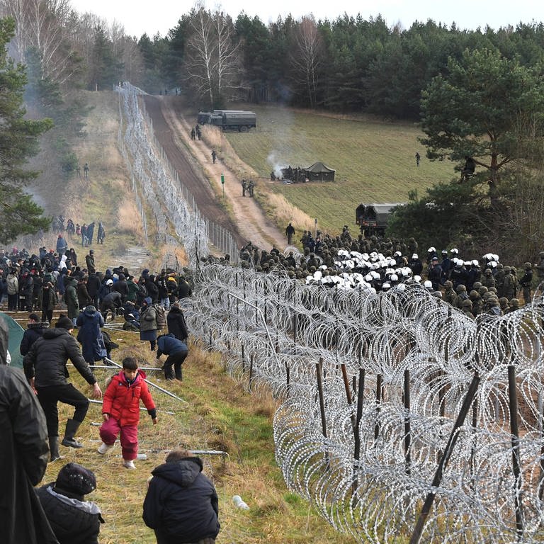 Polnische Polizisten und Soldaten (rechts) bewachen am 8.11.2021 die Grenze in der Nähe eines Migrantenlagers an der weißrussisch-polnischen Grenze in der Region Grodno  Belarus. Hunderte von Migranten aus dem Nahen Osten und Nordafrika versuchten, die Grenze von Weißrussland nach Polen zu überwinden. Aus Sicht der EU benutzt Belarus die Flüchtlinge, um Druck auf die EU auszuüben. (Foto: IMAGO, IMAGO / SNA)