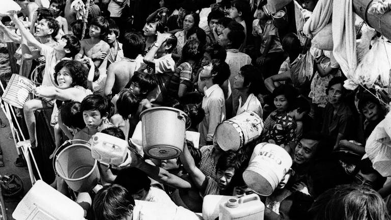 Vietnamesische "Boat People" an Bord des Flüchtlingsschiffs "Tung An" halten den Besatzungsmitgliedern eines Schiffes der philippinischen Marine, das am 21. Februar 1979 mit frischem Trinkwasser anlegte, Eimer und Kanister hin. Seit acht Wochen sitzen die Flüchtlinge an Bord der Tung An in der Bucht von Manila fest. (Foto: picture-alliance / Reportdienste, picture alliance / Associated Press)