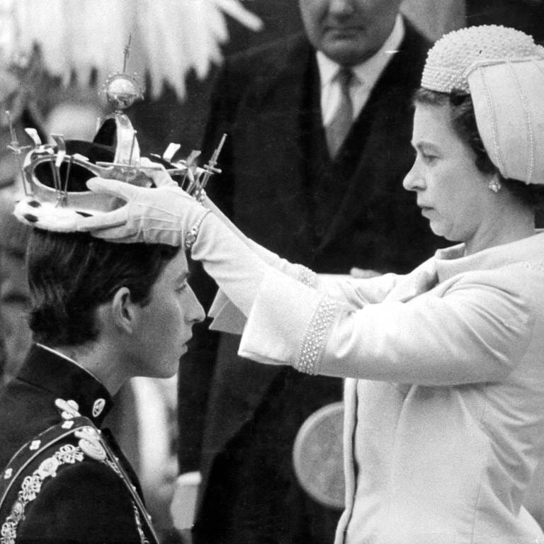 Charles kniet bei seiner Invesitur zum Prince of Wales am 1. Juli 1969 vor seiner Mutter, Elizabeth II, als die Queen im die juwelenbesetzte Goldkrone in Caernarfon Castle auf den Kopf setzt (Foto: IMAGO, IMAGO / United Archives International)
