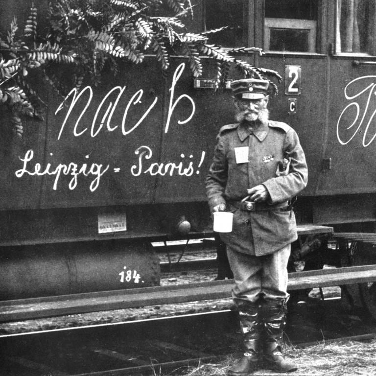 Soldat im Ersten Weltkrieg vor einem Zug mit der Aufschrift "Nach Paris – Leipzig  Paris!" (Foto: IMAGO, IMAGO / Photo12)