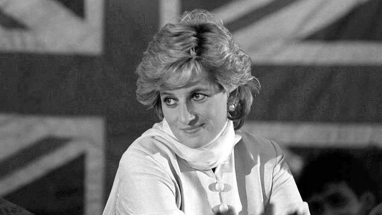 Schwarz-weiß Aufnahme von Lady Diana, die vor einer großen Flagge von England sitzt. (Foto: dpa Bildfunk, Picture Alliance)