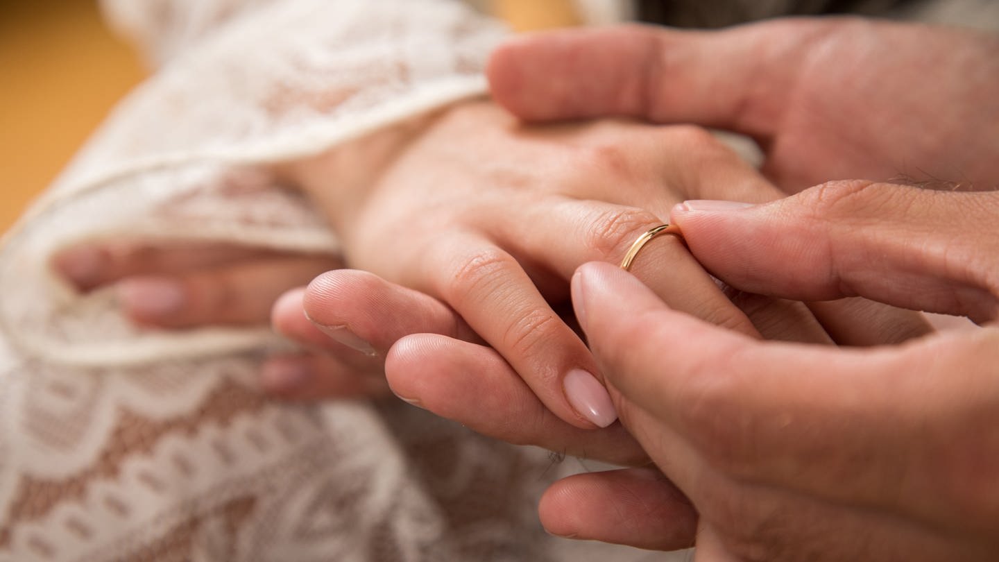 Ein Mann steckt seiner Frau den Ehering an den Ringfinger (Foto: picture-alliance / Reportdienste, dpa Themendienst | Christin Klose)