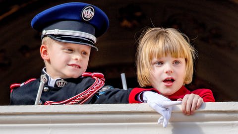 Prinz Jaques und seine Zwillingsschwester Prinzessin Gabriella von Monaco stehen auf einem Balkon, lehnen am Geländer und beobachten am Nationalfeirtag etwas mit großem Interesse. (Foto: picture-alliance / Reportdienste, picture alliance / Royal Press Europe | Albert Nieboer)