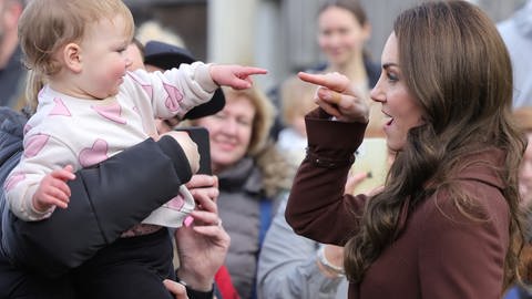 Kate, Prinzessin von Wales in der Menge: Ein kleines Kind auf dem Arm einer Frau streckt den kleinen Finger zu ihr aus und sie reagiert mit ihrem Zeigefinger zurück.  (Foto: picture-alliance / Reportdienste, Picture Alliance)