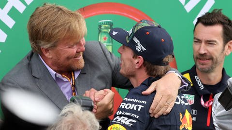 König Willem-Alexander freut sich mit Formel-1-Fahrer Max Verstappen über seinen Sieg beim Großen Preis der Niederlande in Zandvoort. Er legt dem Rennfahrer den Arm um die Schulter und drückt herzlich seine Hand.