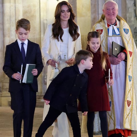 Eine Familie steht mit zwei Geistlichen vor einer Kirche, der kleine Junge in der Mitte pustet die Kerze seiner Schwester aus - Prinz Louis, Princess Charlotte (Foto: picture-alliance / Reportdienste, Picture Alliance)