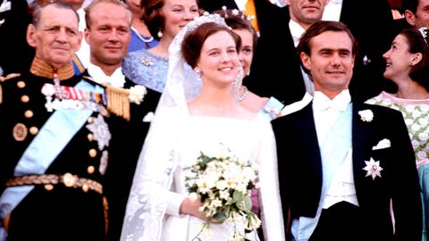 Königin Margrethe II. mit ihrem Ehemann Prinz Henrik von Dänemark bei ihrer Hochzeit. Links neben der damaligen Kornprinzessin steht ihr Vater König Frederik IX. Sie sehen glücklich aus. Margethe trägt ein weißes Hochzeitskleid und ihre Brautstrauß ist ebenfalls weiß.