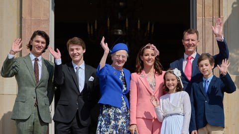 Königin Margrethe mit ihrem jüngeren Sohn Prinz Joachim, dessen aktueller Frau Marie, ihren beiden Kindern und seinen beiden älteren Söhnen aus erster Ehe winken lächelnd in die Kamera.